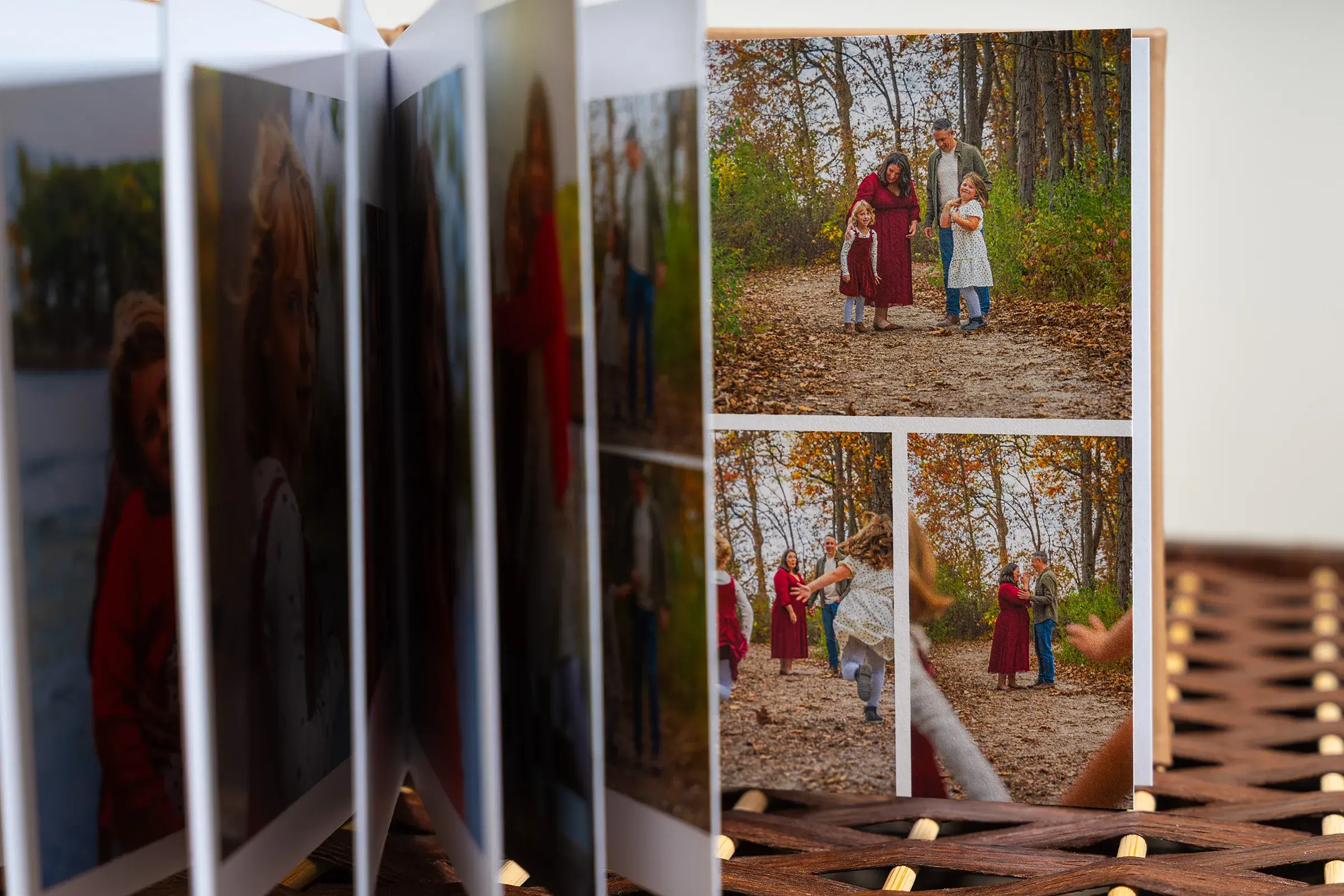 An open photobook on a wicker surface, showing pages of family photos taken outdoors amid autumn foliage.